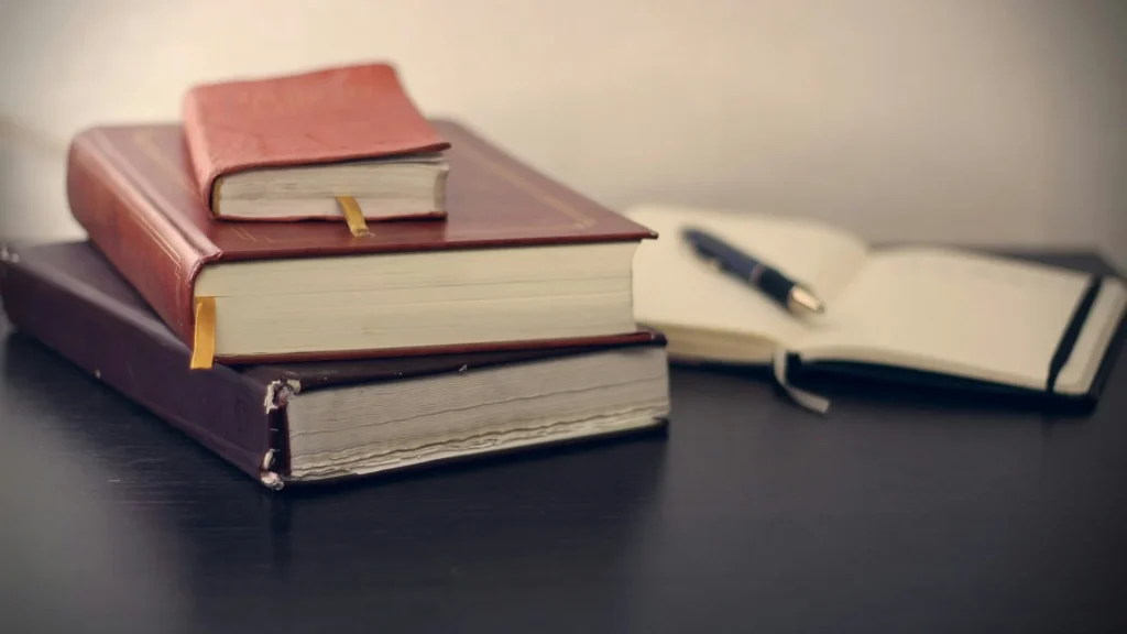 Stack of books beside an open notebook and pen