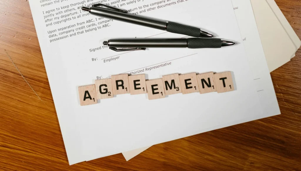 Pens on a document with letter tiles spelling “Agreement”